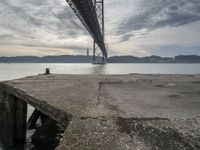 an empty pier at a bridge and water underneath it in the foreground and blue sky