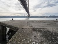 an empty pier at a bridge and water underneath it in the foreground and blue sky