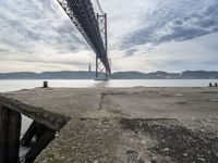 an empty pier at a bridge and water underneath it in the foreground and blue sky