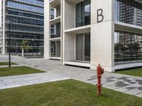 a red fire hydrant in front of a big building with windows next to it