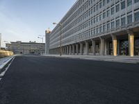 an empty street leads to the side of a large building with columns along it's sides