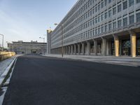 an empty street leads to the side of a large building with columns along it's sides