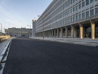 an empty street leads to the side of a large building with columns along it's sides