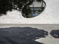 a woman is talking on the phone walking by a building and trees with round windows