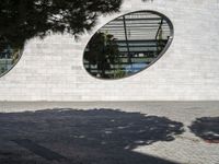 a woman is talking on the phone walking by a building and trees with round windows