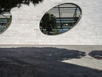 a woman is talking on the phone walking by a building and trees with round windows