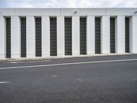 an empty street with no traffic in the distance next to a wall with striped shutter