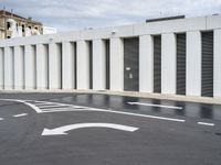 the empty parking lot has two road signs on it's sides and white columns