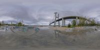 a skate park with a bridge and sky in the background taken through a fish - eye lens