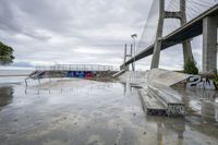 a skate park with ramps at the bottom and some graffiti in the background near a large bridge