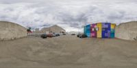 several parked cars in the street of some concrete building near a parking lot with multiple identical building