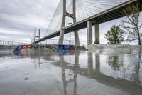 a skate park under a bridge with graffiti on it's wall and in the ground is a river