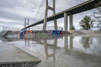 a skate park under a bridge with graffiti on it's wall and in the ground is a river