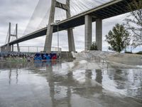 a bridge is shown behind some people on skateboards, while others watch him,