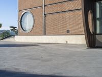 a person with a skateboard in front of a building near the water, and one person walking on a sidewalk and one person with a skateboard