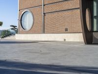 a person with a skateboard in front of a building near the water, and one person walking on a sidewalk and one person with a skateboard