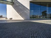 there is an empty bench on the sidewalk in front of the large building with a reflection of it