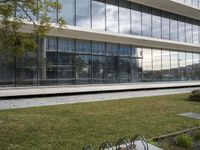 a woman stands in front of a large building with glass walls and trees in the grass