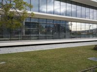 a woman stands in front of a large building with glass walls and trees in the grass