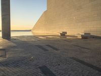 a shadow on an empty concrete area with some benches near by the water and two concrete pillars