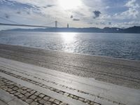 a picture of someone sitting on the beach in the sun at a beach with a bridge over the water and the sea behind it