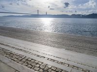 a picture of someone sitting on the beach in the sun at a beach with a bridge over the water and the sea behind it