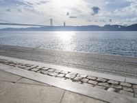 a picture of someone sitting on the beach in the sun at a beach with a bridge over the water and the sea behind it