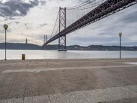 a lone person is sitting on the edge of a dock by the water in front of the bridge