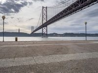 a lone person is sitting on the edge of a dock by the water in front of the bridge