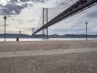 a lone person is sitting on the edge of a dock by the water in front of the bridge