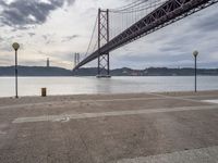 a lone person is sitting on the edge of a dock by the water in front of the bridge