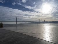 the sky is partly cloudy over the bridge and water near the ocean flooring stone walkway