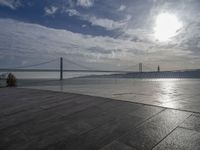 the sky is partly cloudy over the bridge and water near the ocean flooring stone walkway