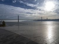 the sky is partly cloudy over the bridge and water near the ocean flooring stone walkway