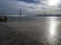 the sky is partly cloudy over the bridge and water near the ocean flooring stone walkway