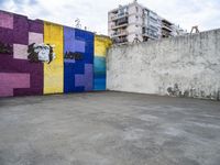 colorful wall with large graffiti artwork in a empty parking lot at an alleyway with building to the side