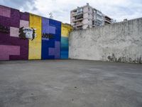 colorful wall with large graffiti artwork in a empty parking lot at an alleyway with building to the side