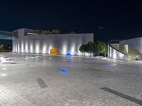 several benches and benches in the open with lights at night on their legs near buildings