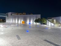 several benches and benches in the open with lights at night on their legs near buildings