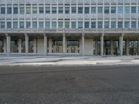 a large building with windows on the side of a road by itself and with people standing outside the doors