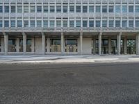 a large building with windows on the side of a road by itself and with people standing outside the doors