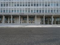 a large building with windows on the side of a road by itself and with people standing outside the doors