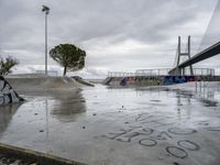 a concrete skateboarder does a trick on the ramp near a pedestrian bridge and some cars