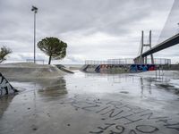 a concrete skateboarder does a trick on the ramp near a pedestrian bridge and some cars