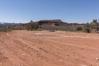 an empty dirt road in a rocky desert valley with trees in front of it and mountains in the back ground