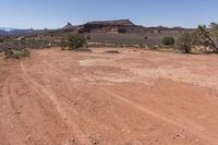 an empty dirt road in a rocky desert valley with trees in front of it and mountains in the back ground