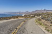 the road in front of a body of water with a dirt road at both sides