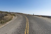 two lane road going uphill with mountain in the distance under blue sky with no clouds