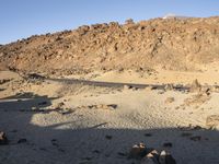 a lone black truck on the side of a desert road near a mountain and sign