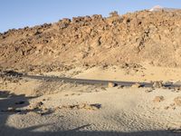 a lone black truck on the side of a desert road near a mountain and sign